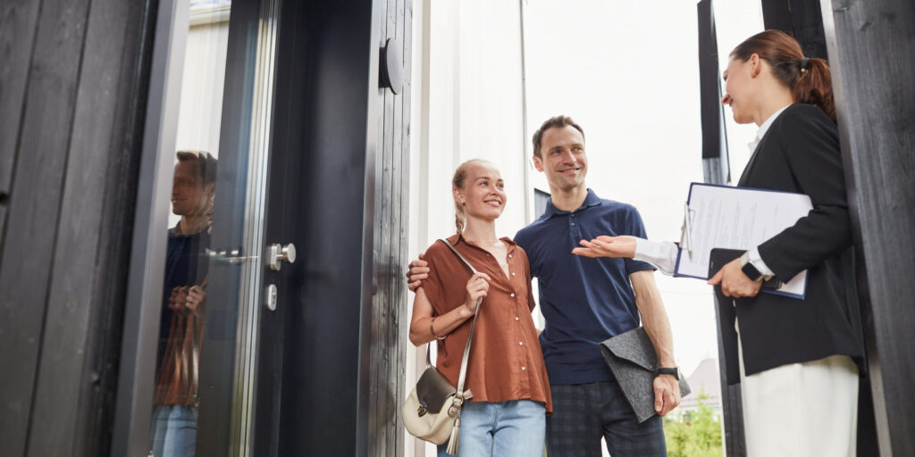 Waist up portrait of female real estate agent meeting young couple standing in doorway while buying new house, copy space