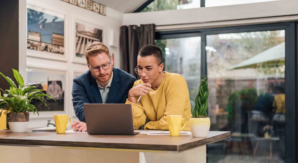 Young successful mixed races couple sitting in living room or kitchen discussing new home project using laptop working and planing calculating home finances doing paperwork stressed about problems
