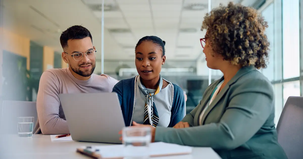 Three colleagues having a discussion while viewing a laptop screen in a bright, modern office." Let me know if you'd like to refine this further!